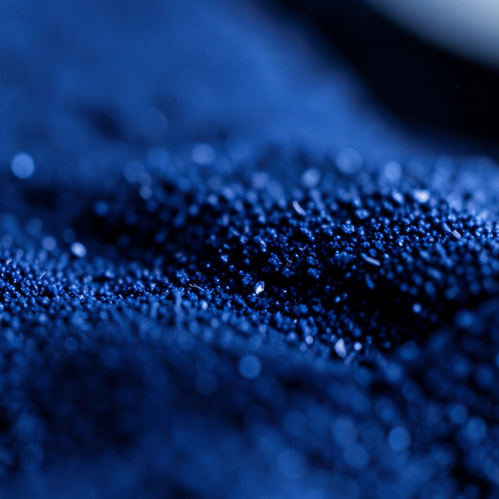 Extreme close-up photograph of a brushed metallic circuit board surface in deep navy and slate tones with subtle gold traces, conveying an industrial hardware feel.